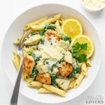 An overhead shot of a white bowl filled with creamy artichoke spinach chicken pasta, set on a marble surface.