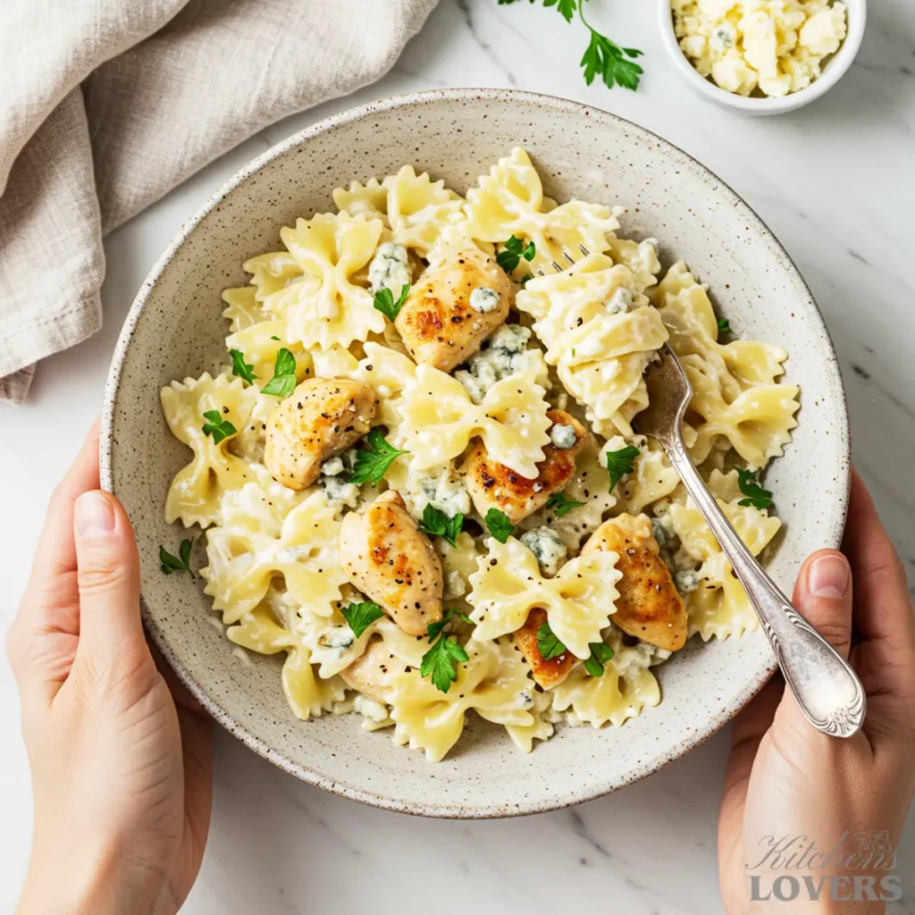 A rustic stoneware bowl filled with creamy chicken and farfalle pasta in a gorgonzola sauce, garnished with fresh parsley.