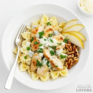A white bowl filled with creamy chicken gorgonzola pasta with farfalle noodles. The dish is garnished with fresh parsley and served with fresh pear slices and walnuts on the side.