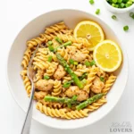 Overhead photo of chipotle chicken pasta in a white bowl on a marble surface, with parmesan and green onions on the side.