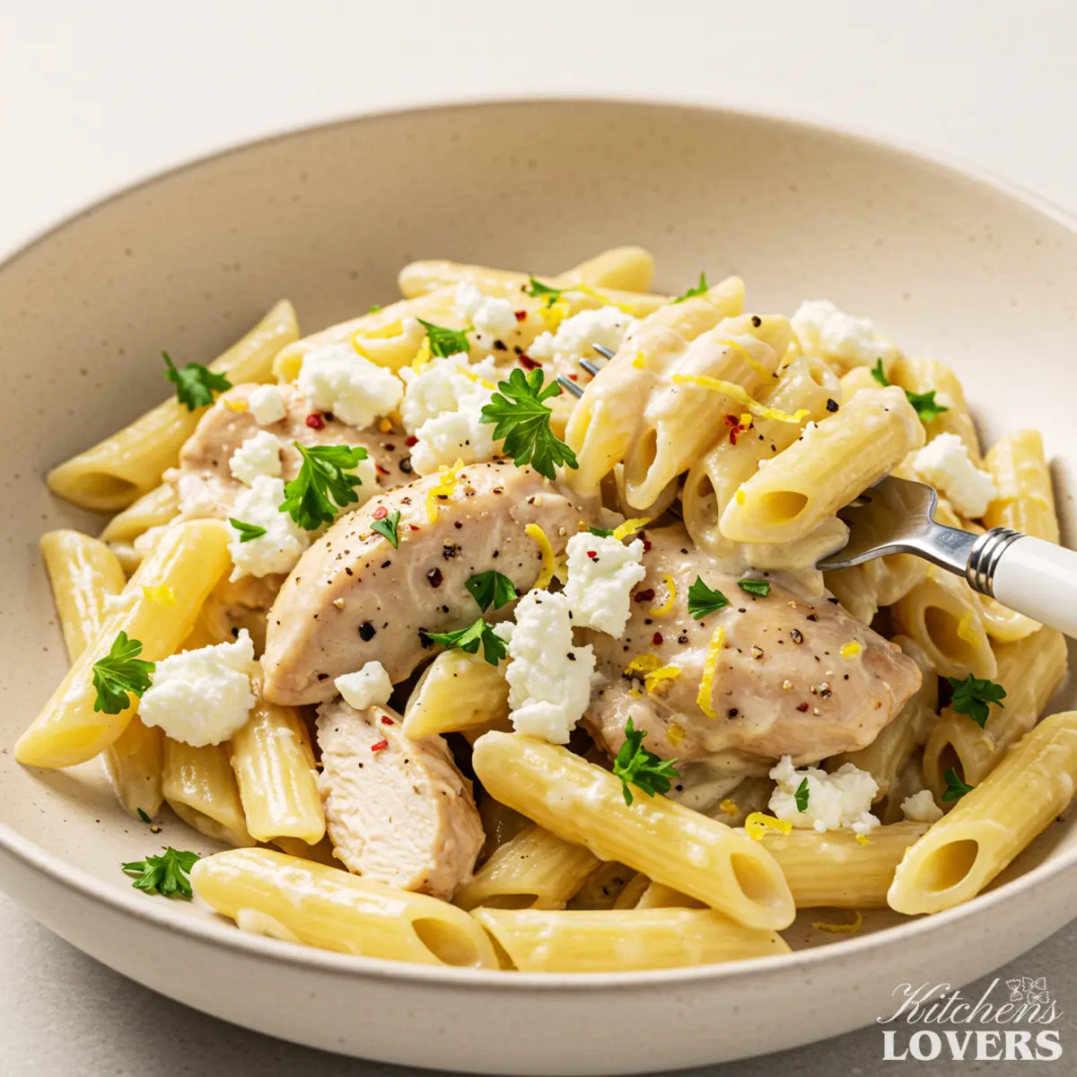 Close-up of creamy goat cheese pasta with chicken, fresh parsley, and lemon zest in a white bowl.