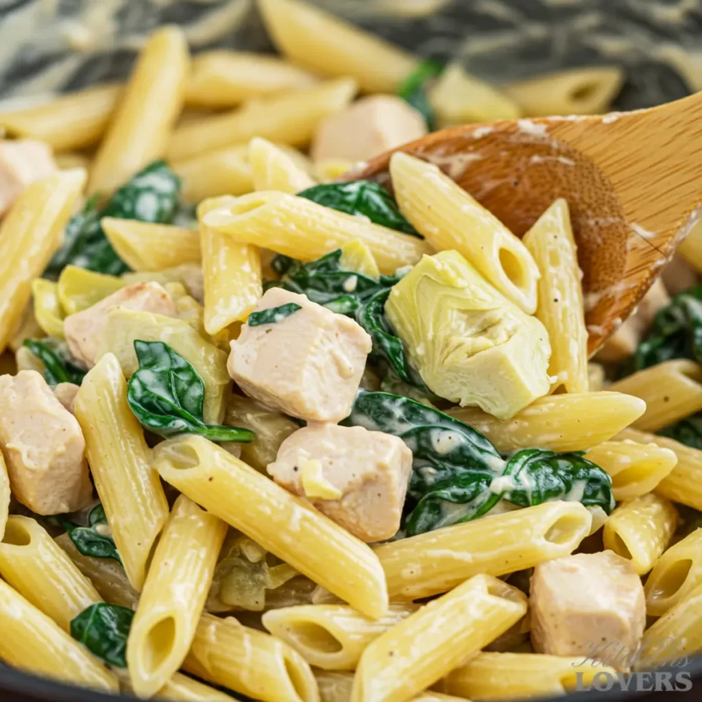 A close-up shot of creamy chicken and spinach pasta being stirred with a wooden spoon in a skillet.