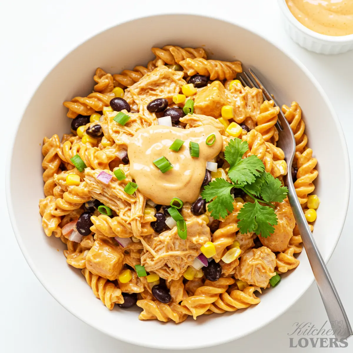 An overhead shot of a large white bowl filled with creamy BBQ chicken pasta salad, garnished with fresh cilantro and paprika. A fork is in the bowl.