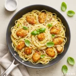 A top-down photo of creamy Chicken Carbonara with golden chicken, fresh basil, and grated cheese in a dark skillet.