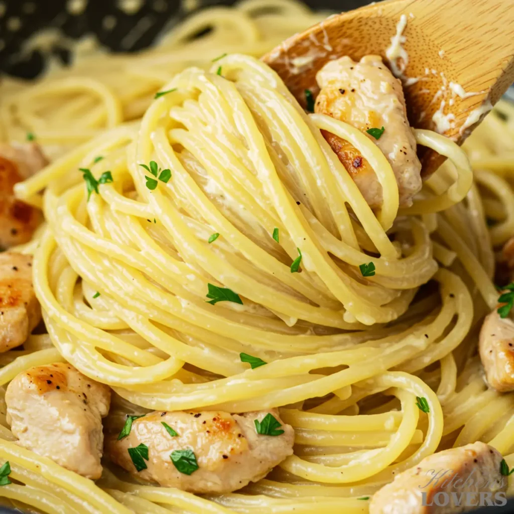 A close-up macro photograph of creamy chicken carbonara being mixed in a bowl with a wooden spoon, showing the sauce coating the pasta.