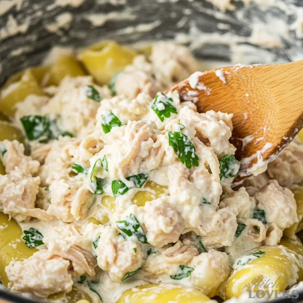 A close-up macro shot of a wooden spoon mixing a creamy filling of shredded chicken, ricotta cheese, and herbs in a bowl.
