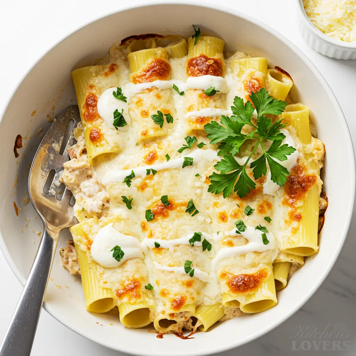 Overhead view of a white ceramic baking dish filled with creamy chicken manicotti, topped with melted mozzarella cheese and fresh parsley.