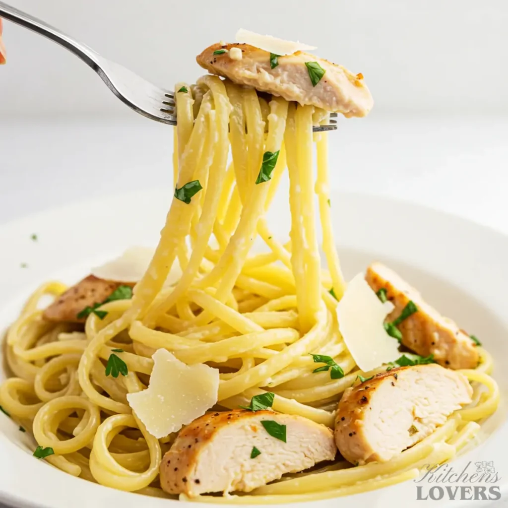 A fork twirling pasta and lifting a tender piece of chicken from a dish.
