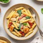 A top-down photo of creamy Tuscan chicken pasta in a rustic bowl, garnished with fresh basil and Parmesan cheese.