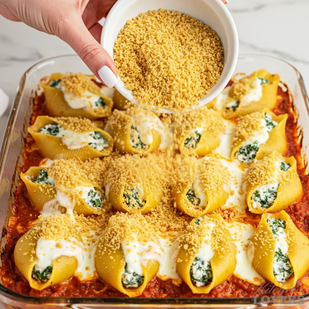 kate hands sprinkling golden, toasted panko breadcrumbs over a casserole of stuffed shells that is already topped with hot, melted mozzarella cheese.