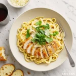 A top-down photo of homemade Chicken Alfredo from Scratch with seared chicken, fettuccine, and fresh herbs.