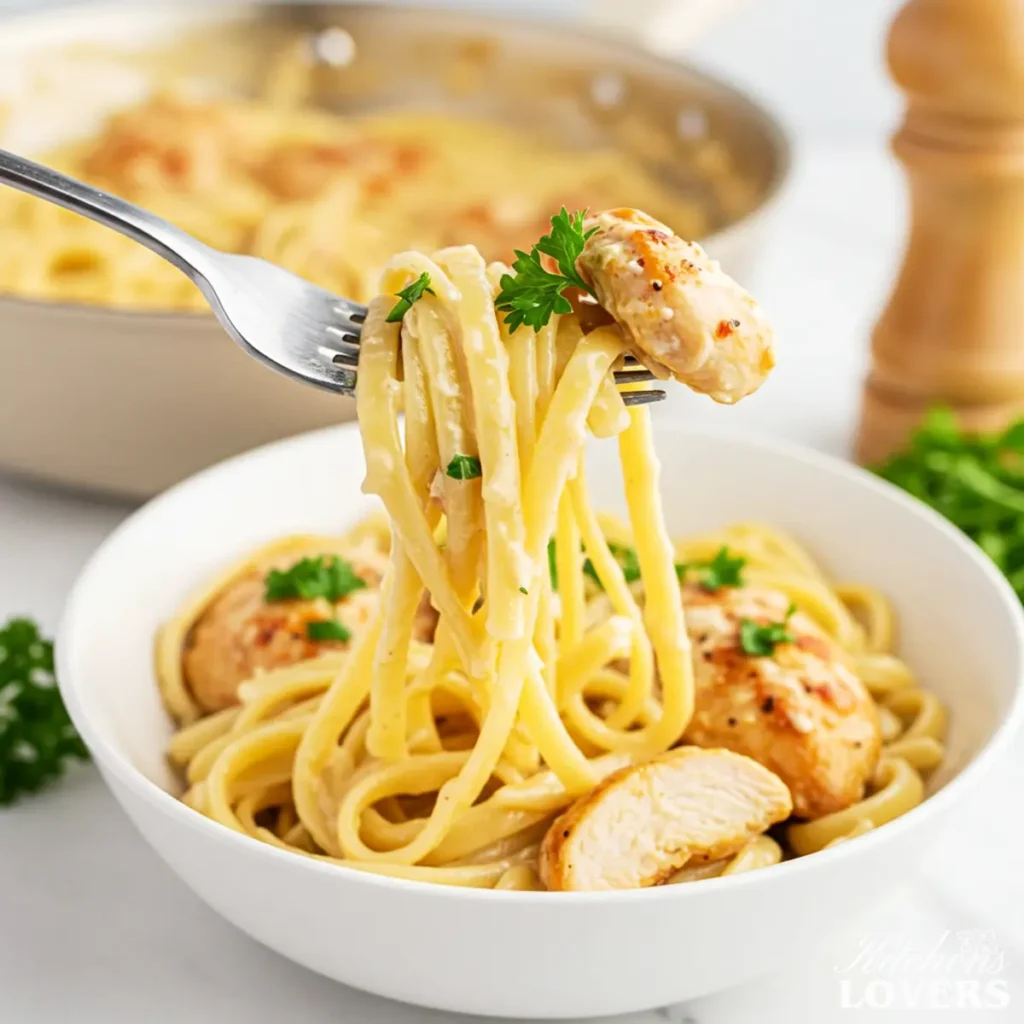 A close-up shot of a fork lifting a perfect bite of creamy Chicken Lazone pasta from a white bowl, showing the linguine coated in sauce with a piece of chicken.	