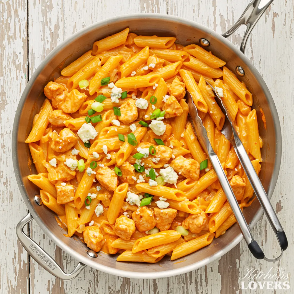 A top-down photo of creamy Buffalo chicken pasta in a skillet, garnished with blue cheese and green onions.